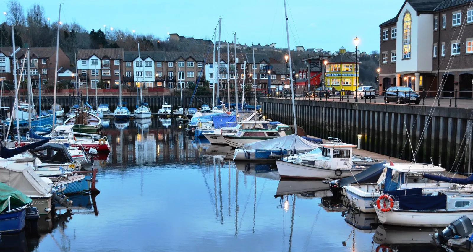 St Peters Basin at dusk, with boats on the pontoons, lights reflected in the water and the yellow marina office beyond